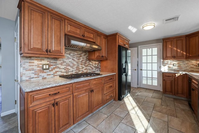 kitchen with decorative backsplash, black fridge with ice dispenser, stainless steel gas stovetop, and range hood