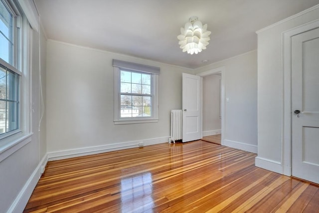 empty room featuring a notable chandelier, radiator heating unit, ornamental molding, and light wood-type flooring