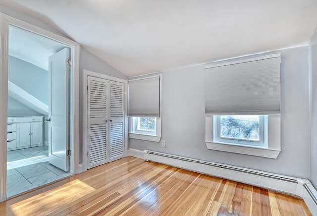 interior space featuring a baseboard radiator, light hardwood / wood-style floors, and vaulted ceiling