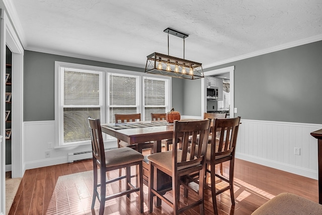 dining area with hardwood / wood-style floors, ornamental molding, a textured ceiling, and a baseboard heating unit