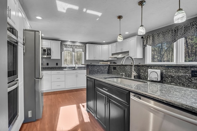 kitchen featuring dark stone counters, stainless steel appliances, sink, white cabinets, and hardwood / wood-style floors