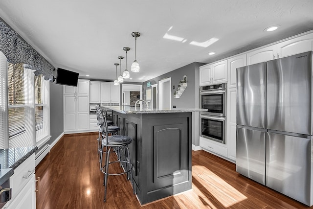 kitchen with a center island with sink, white cabinets, light stone countertops, appliances with stainless steel finishes, and decorative light fixtures