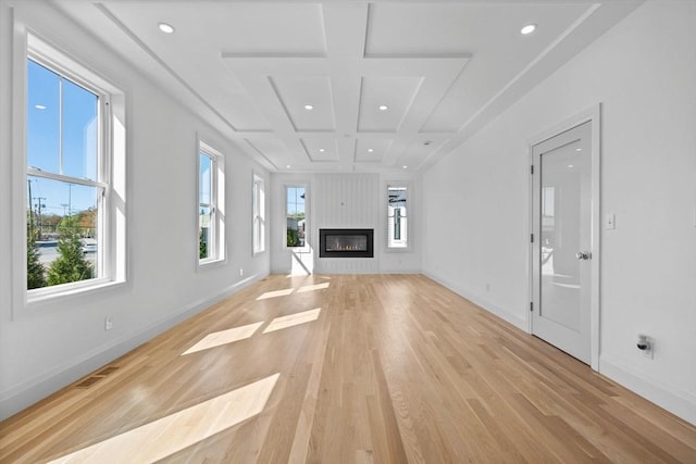 unfurnished living room featuring coffered ceiling, light wood-type flooring, recessed lighting, baseboards, and a glass covered fireplace