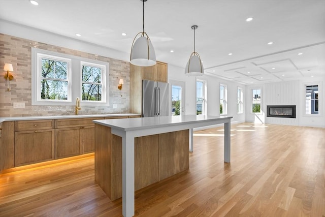 kitchen featuring high end fridge, a sink, brown cabinetry, light countertops, and light wood-type flooring