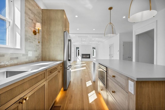 kitchen with open floor plan, light wood-style floors, stainless steel refrigerator, brown cabinets, and light countertops