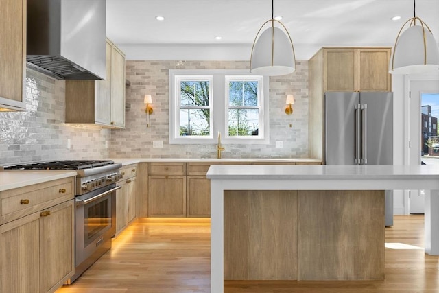 kitchen with high end appliances, wall chimney exhaust hood, a sink, light wood-type flooring, and recessed lighting