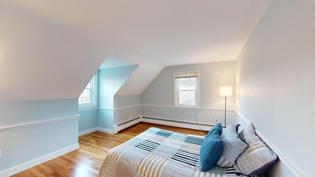 bedroom with a baseboard heating unit, light hardwood / wood-style flooring, and multiple windows