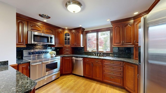 kitchen with backsplash, dark stone counters, sink, light hardwood / wood-style floors, and stainless steel appliances