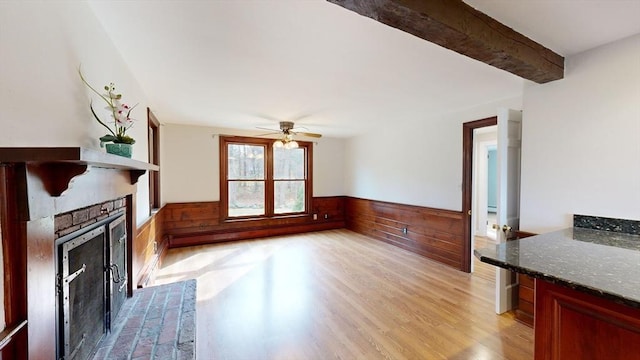 unfurnished living room with beamed ceiling, ceiling fan, wood walls, and light wood-type flooring