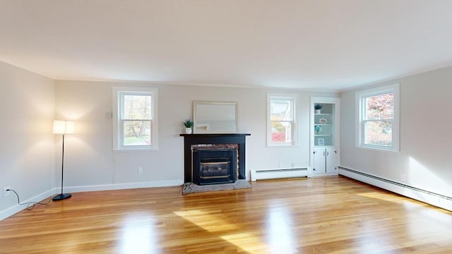 unfurnished living room with light wood-type flooring, a baseboard heating unit, and a healthy amount of sunlight