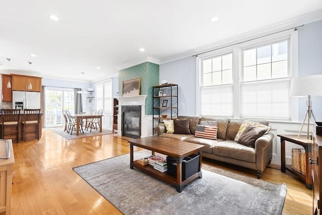 living area with crown molding, light wood-type flooring, a glass covered fireplace, and recessed lighting