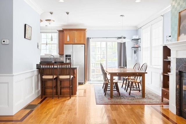 dining room featuring crown molding, a high end fireplace, light wood-type flooring, wainscoting, and a decorative wall