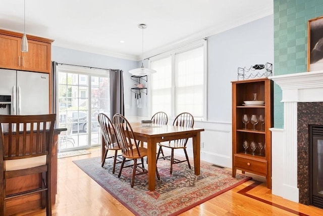 dining area with a fireplace, crown molding, and light wood finished floors
