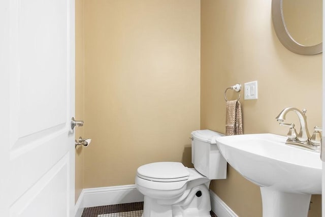 half bathroom featuring a sink, toilet, baseboards, and tile patterned floors