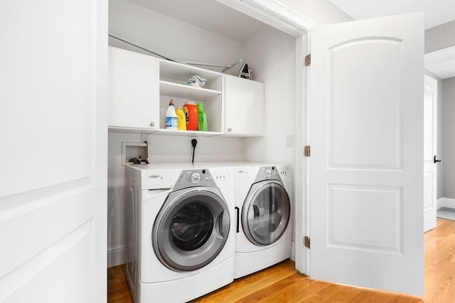 clothes washing area with cabinet space, washing machine and clothes dryer, and light wood-style flooring