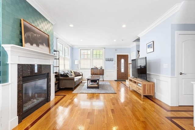 living area featuring ornamental molding, light wood-style floors, a premium fireplace, wainscoting, and a decorative wall