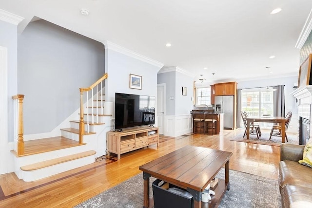 living room with crown molding, light wood finished floors, stairway, recessed lighting, and a wainscoted wall