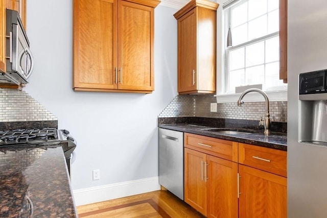 kitchen with stainless steel appliances, a sink, backsplash, baseboards, and wood finished floors