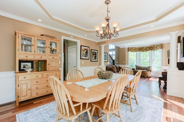 dining area with decorative columns, a wainscoted wall, crown molding, light wood-type flooring, and a chandelier