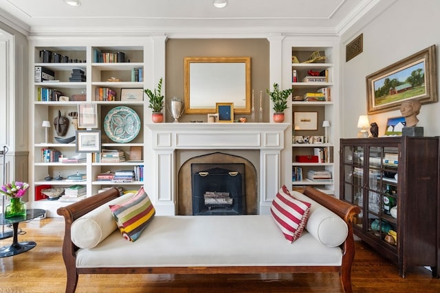 living room with wood-type flooring, built in shelves, and ornamental molding