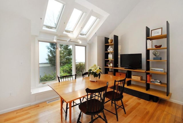 dining area with vaulted ceiling with skylight and light wood-type flooring