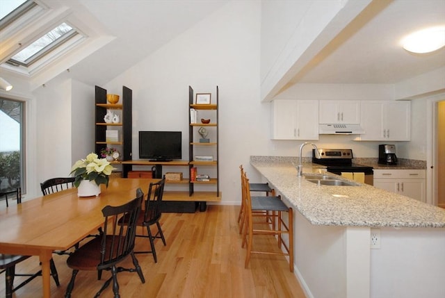 kitchen featuring a breakfast bar area, electric range, light stone counters, white cabinets, and kitchen peninsula