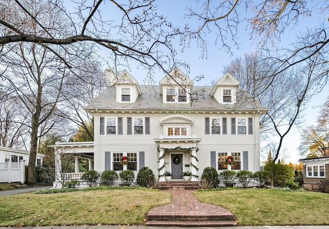 colonial house featuring stucco siding, a chimney, and a front yard