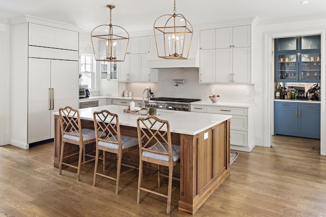 kitchen featuring light countertops, paneled built in fridge, a kitchen island with sink, and white cabinets