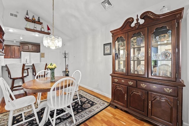 dining space with vaulted ceiling, a chandelier, and light hardwood / wood-style floors