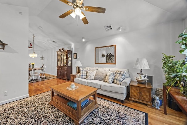 living room with ceiling fan with notable chandelier, vaulted ceiling, and light wood-type flooring