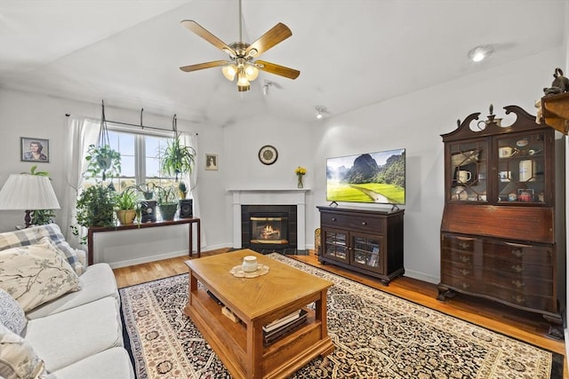 living room with wood-type flooring, a tiled fireplace, vaulted ceiling, and ceiling fan