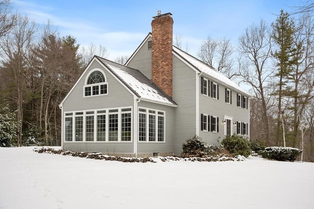 snow covered rear of property with a sunroom