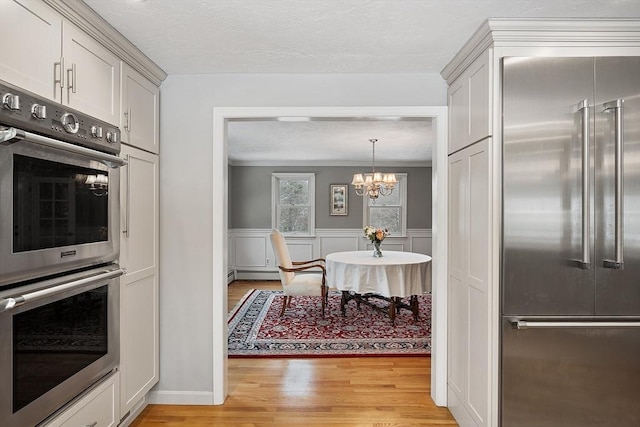 kitchen featuring a chandelier, appliances with stainless steel finishes, light hardwood / wood-style floors, ornamental molding, and a baseboard heating unit