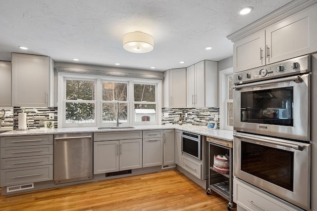 kitchen with stainless steel appliances, light hardwood / wood-style floors, backsplash, and gray cabinetry