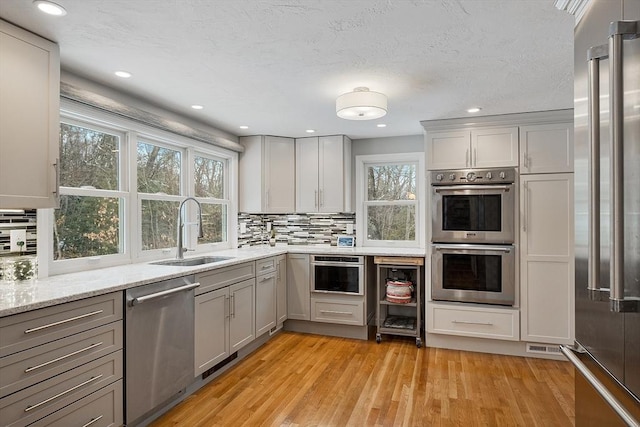 kitchen featuring stainless steel appliances, light hardwood / wood-style floors, tasteful backsplash, gray cabinetry, and sink