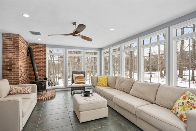 sunroom / solarium with ceiling fan, a wealth of natural light, and a wood stove