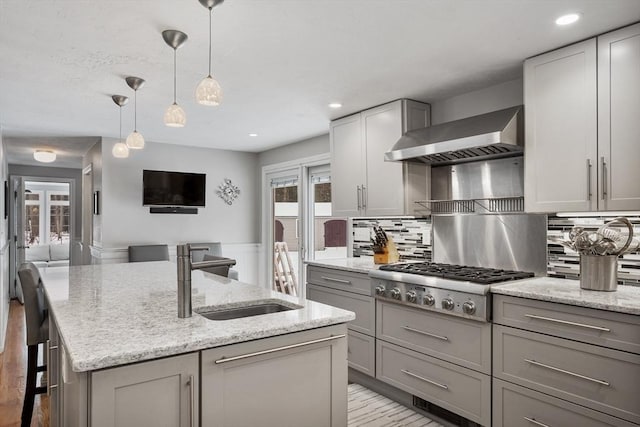 kitchen with sink, tasteful backsplash, stainless steel gas stovetop, a center island with sink, and wall chimney range hood