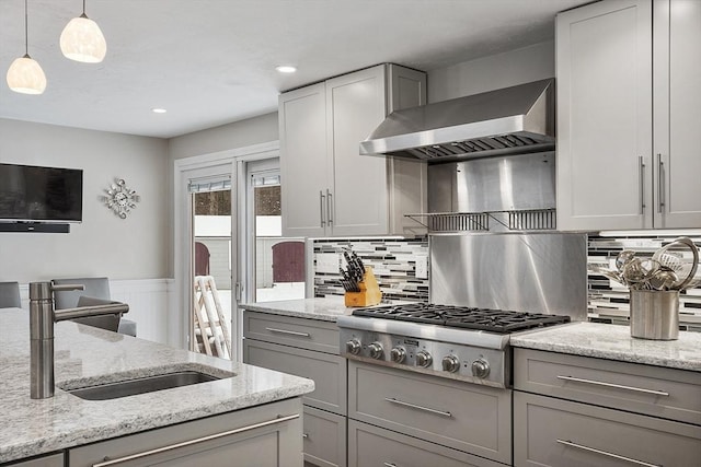 kitchen featuring light stone counters, pendant lighting, wall chimney range hood, stainless steel gas cooktop, and gray cabinets