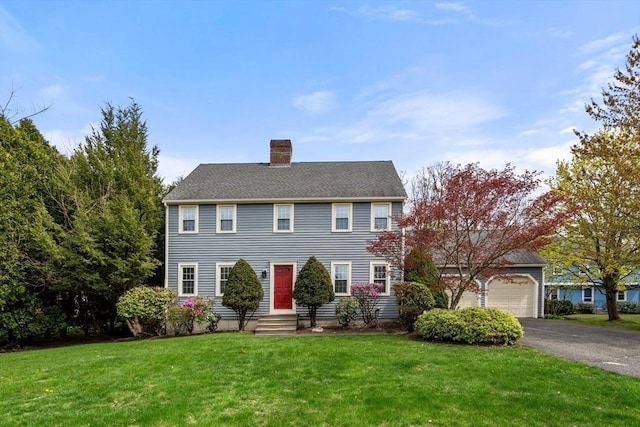 colonial home featuring a chimney, a front lawn, driveway, and an attached garage
