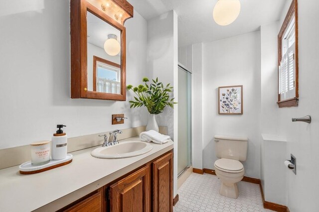 full bathroom featuring vanity, toilet, a stall shower, and baseboards