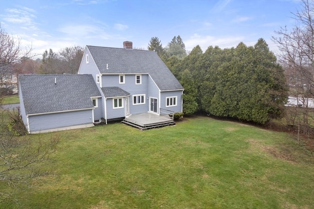 back of house with a lawn, roof with shingles, a chimney, and a deck