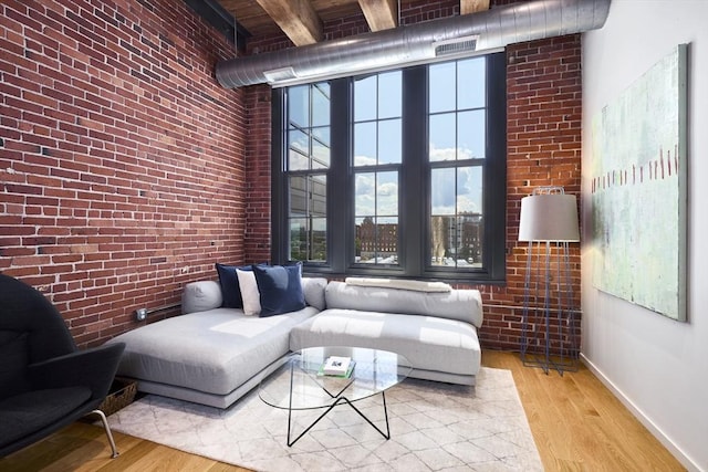 living room with brick wall, a high ceiling, and light wood-type flooring