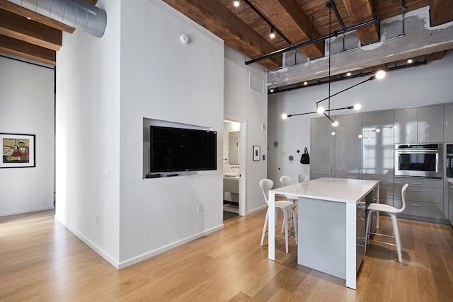 kitchen with a breakfast bar area, gray cabinetry, hanging light fixtures, beamed ceiling, and oven