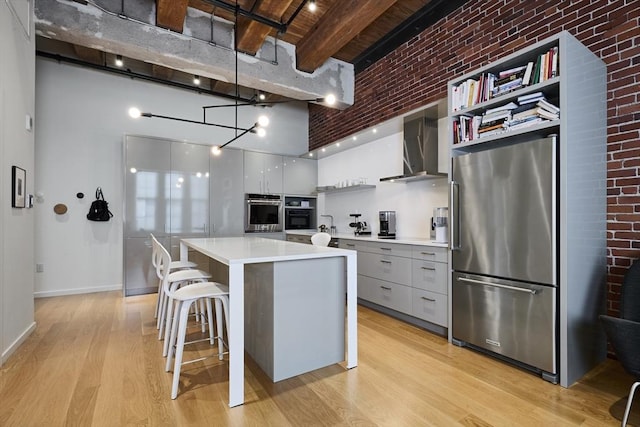 kitchen with decorative light fixtures, wall chimney range hood, a kitchen island, beam ceiling, and high end fridge