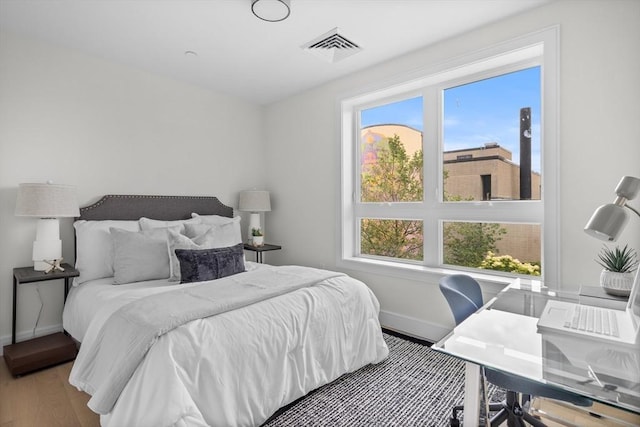 bedroom featuring baseboards, multiple windows, wood finished floors, and visible vents