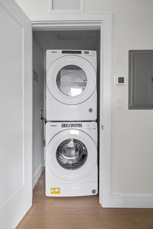laundry room with visible vents, laundry area, baseboards, stacked washing maching and dryer, and electric panel