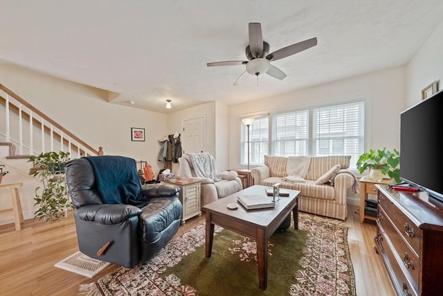 living room featuring a ceiling fan, stairway, and light wood finished floors