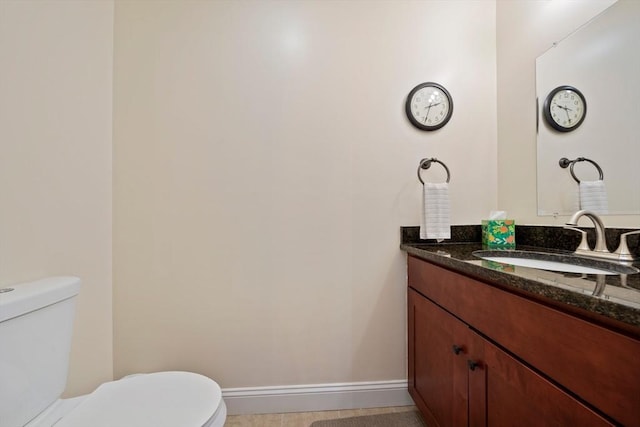 half bath with toilet, baseboards, and vanity