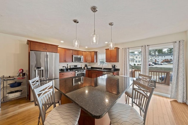 kitchen with light wood-style flooring, appliances with stainless steel finishes, hanging light fixtures, a kitchen bar, and a sink