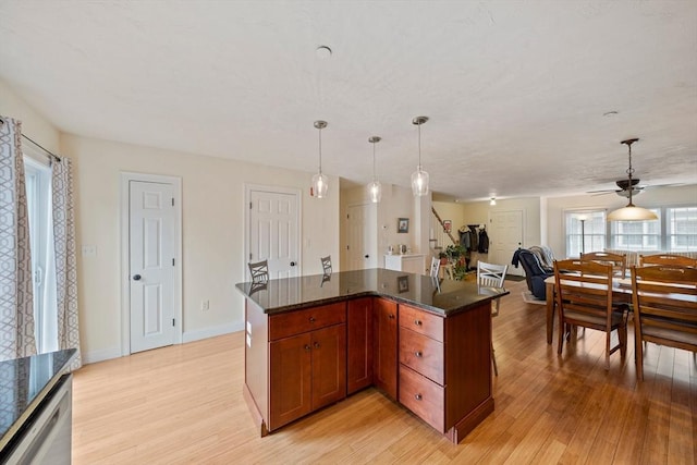 kitchen with baseboards, open floor plan, dark stone countertops, light wood-style floors, and pendant lighting